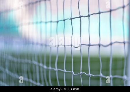 Soccer goal net close-up with blurred field and stadium, creating an abstract sporting background Stock Photo