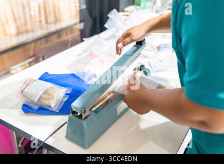 The officer sealing a package using a manual heat sealer, commonly used for preserving goods. Stock Photo
