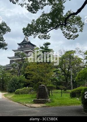 Hiroshima Castle in Japan, surrounded by lush green trees on a cloudy day. Stock Photo