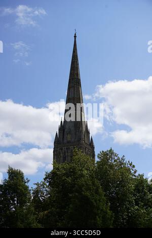 Historic Church Spire Against Blue Sky with Lush Trees in Foreground. Salisbury, England Stock Photo