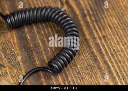 a black cable twisted in the shape of a spring for equipment close up, an old black cable in a rubber braid for connecting different devices Stock Photo