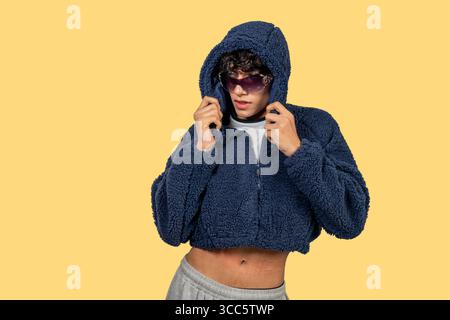 Fashionable young man is posing wearing blue, furry, hooded jacket and sunglasses Stock Photo