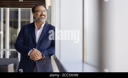 Cheerful successful mature Indian CEO man looking out of window Stock Photo