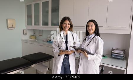 Two successful Latin doctor women in lab coats standing together Stock Photo