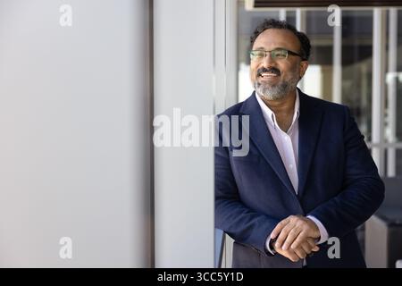 Happy Indian company director man posing at large office window Stock Photo