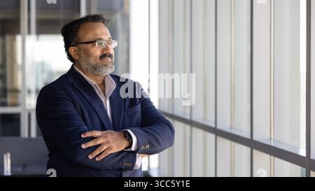 Positive Indian company executive man looking at large office window Stock Photo