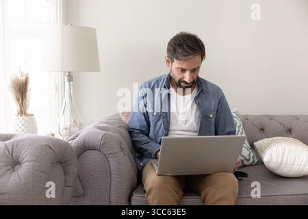 Focused man sitting on sofa with laptop on his lap Stock Photo
