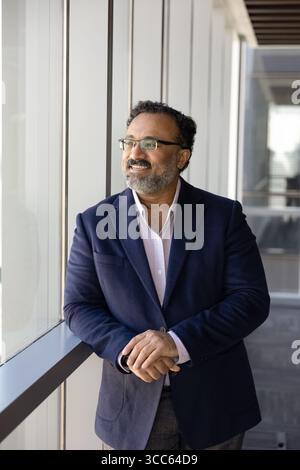 Cheerful positive successful senior Indian executive man standing at window Stock Photo
