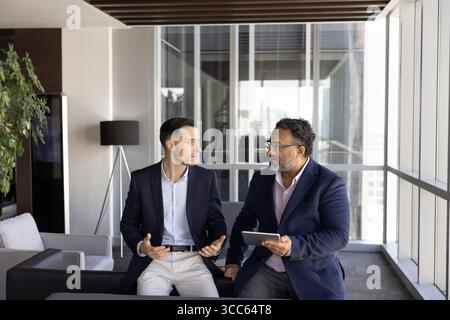 Two younger and elder male business colleagues talking in office Stock Photo