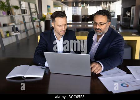 Serious young and senior business partners using laptop at table Stock Photo