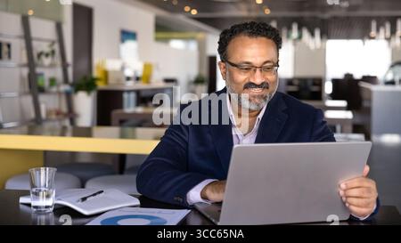 Positive successful senior Indian business professional man typing on laptop Stock Photo