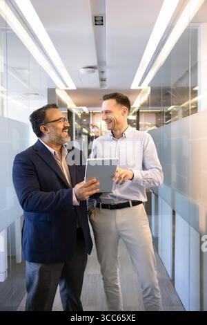 Cheerful diverse business partners using tablet in office corridor Stock Photo