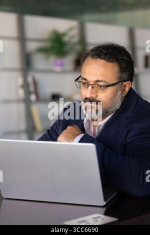 Serious older Indian business professional man working at laptop computer Stock Photo