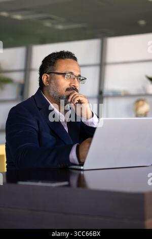 Serious pensive senior Indian CEO man working at laptop Stock Photo