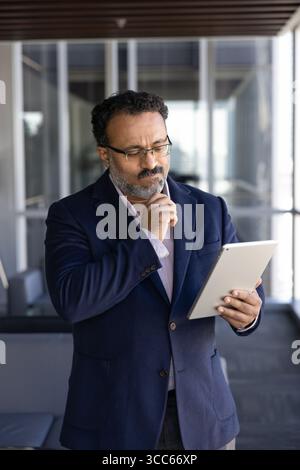 Thoughtful elder Indian CEO man reading or watching online content Stock Photo