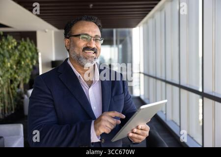 Happy pensive senior business executive man typing on digital tablet Stock Photo
