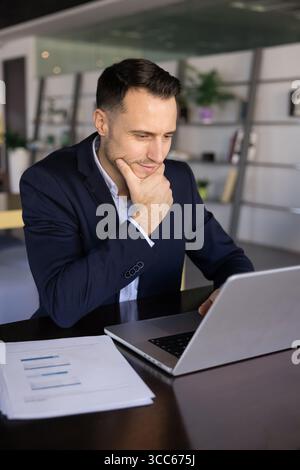 Positive pensive Latin business product owner man typing on laptop Stock Photo