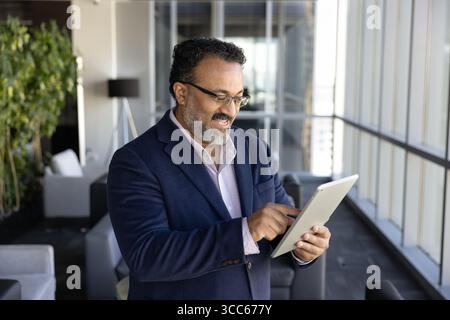 Positive older male Indian CEO using online financial web service Stock Photo