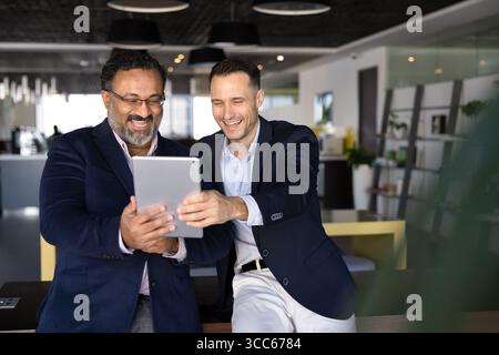 Two excited younger and elder office colleagues using digital tablet Stock Photo