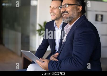 Cheerful multiethnic senior and young male coworkers sitting together Stock Photo