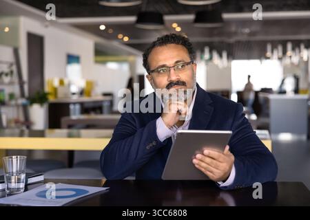 Thoughtful old Indian business man working with tablet in co-working Stock Photo