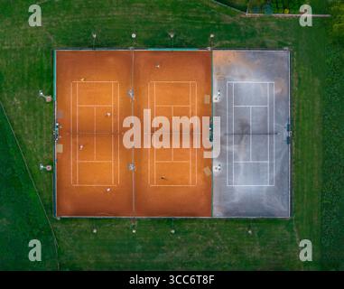 Aerial image of active clay and worn-out hard tennis courts in the middle of green sports complex Stock Photo