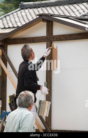 Two experienced craftsmen are painting the corner of a wooden house. The scene captures the meticulous attention to detail required in this traditiona Stock Photo