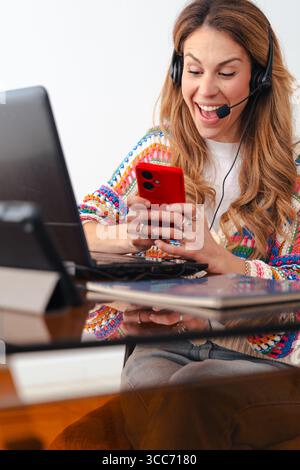 Woman with headset working on laptop and using smartphone at home office Stock Photo