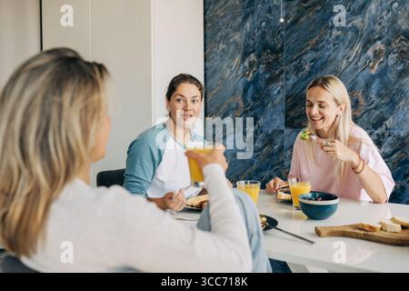 A group of female friends sitting at the table having breakfast and chatting. Stock Photo