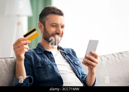 Positive man with smartphone holding credit card Stock Photo