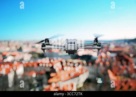 Modern quadcopter flying above cityscape with red rooftops and clear blue sky Stock Photo