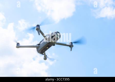 Close-up bottom view of flying drone with camera facing forward under blue sky Stock Photo