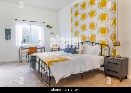 Bright and stylish modern bedroom in white and yellow featuring a metal-framed bed with pillows, desk , and window Stock Photo