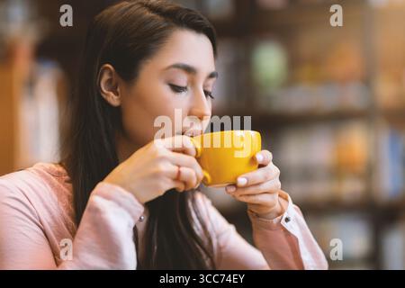 Time for coffee. Carefree arab lady sitting at cafe, holding mug of hot drink and enjoying aroma of coffee Stock Photo