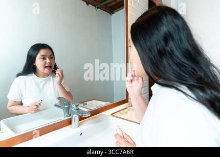 Asian woman standing in front of a bathroom mirror applying lipstick. Self-care and beauty routine in the morning. Stock Photo