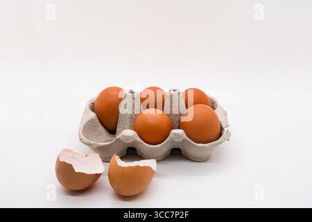 Box of 5 eggs in a cardboard carton with one egg cracked on the side isolated on a white background Stock Photo