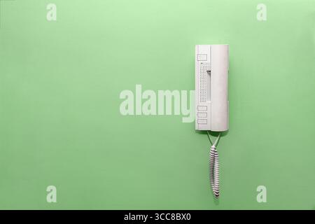 Light plastic intercom with fine gray speckles, buttons, and coiled cord on a light green plastered wall, home communication concept with copy space. Stock Photo