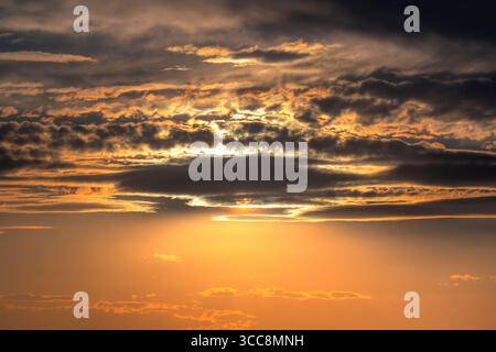 Sky of an orange hue with black clouds surrounded by sun rays. Stock Photo