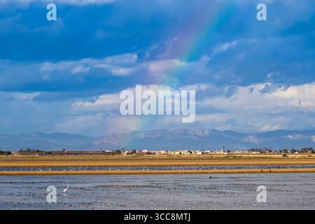 Rainbow over fields and mountains with a village in calm beneath a sky covered by storm clouds Stock Photo