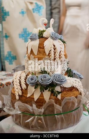 A beautifully decorated two-tier wedding cake featuring delicate swan figurines, intricate white lace detailing, and a cascade of dusty blue roses, pe Stock Photo