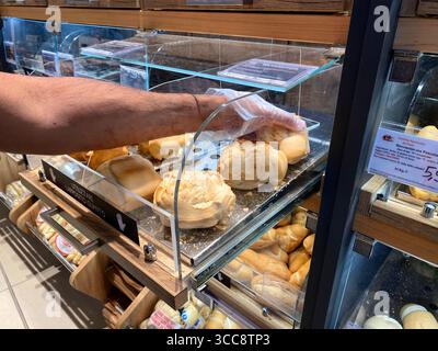 Conselve, Italy - May 16, 2025: Customer's hand is reaching for fresh bread rolls in a bakery display case filled with various baked goods Stock Photo
