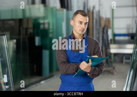 Focused technician inspecting and documenting glass panels in workshop Stock Photo