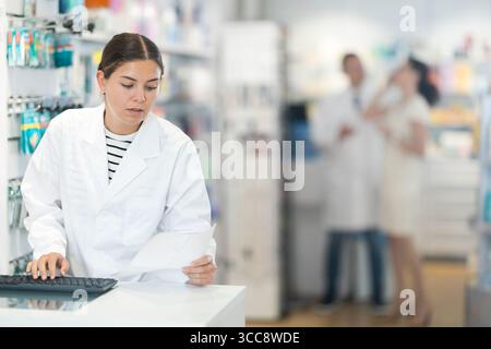 Woman pharmacist looking for prescription medicine using computer Stock Photo