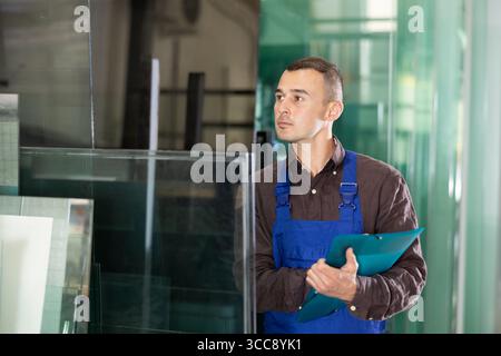Focused technician inspecting and documenting glass panels in workshop Stock Photo