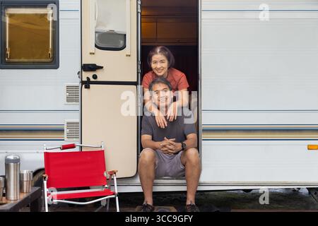Senior asian couple joyful and relax sitting in front of caravan home on vacation. Stock Photo