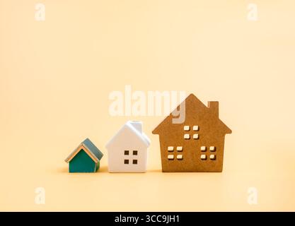 Different sizes of miniature houses on pastel yellow background. Concept for real estate investment, property market, mortgage, living option, housing Stock Photo