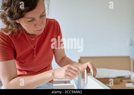 Woman assembling bed frame on wooden floor, using wrench. DIY furniture assembly and home improvement Stock Photo