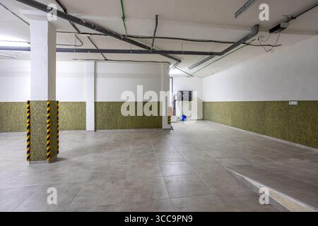 Clean and spacious underground garage with tiled flooring, painted walls, and visible piping, ideal for parking or additional storage. Stock Photo