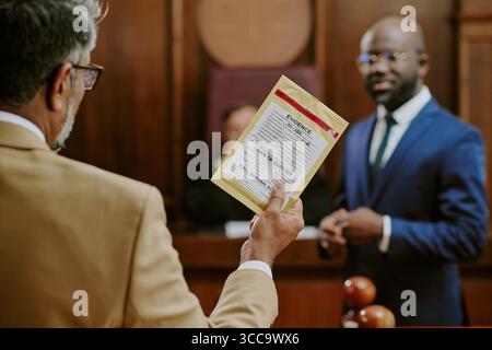 Middle Aged Man Presenting Evidence to Young Adult Black Man in Courtroom Stock Photo