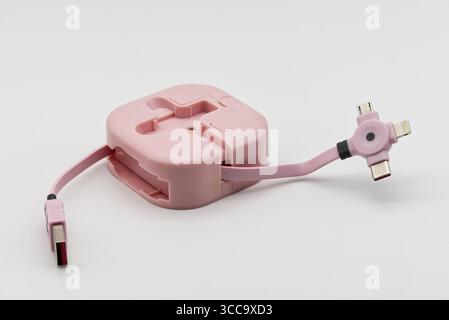 A pink retractable multi-charging cable with various connectors lies on a clean white background, ready for use. Stock Photo